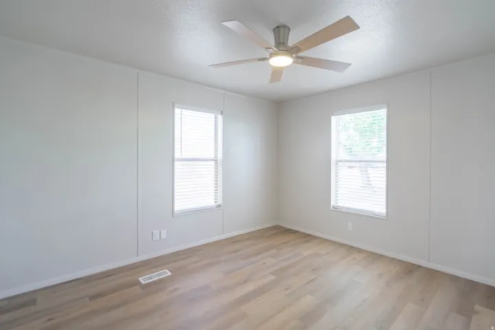 Bedroom featuring two windows with horizontal blinds, wood-finish flooring, and a ceiling fan with integrated lighting