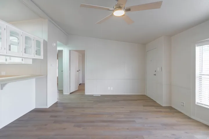 Open-concept living space with wood-finish flooring, white walls, and a contemporary ceiling fan with integrated lighting