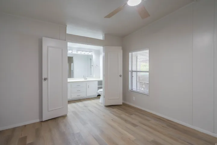 Light wood-finish flooring throughout, featuring a window with blinds and a ceiling fan
