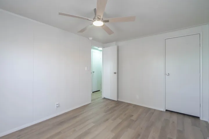 Room featuring wood-finish flooring, white panel walls, and a ceiling fan with integrated lighting