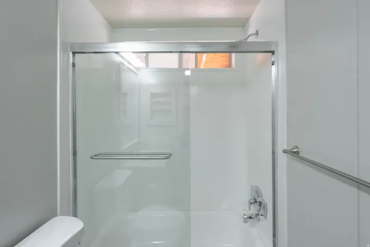 Shower enclosure featuring a sliding glass door, integrated grab bar, overhead showerhead, and wall-mounted plumbing fixtures