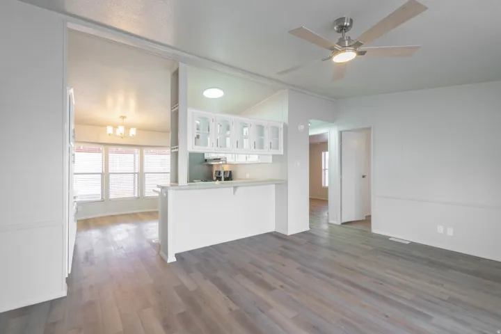 Open-concept living space featuring wood-finish flooring, a ceiling fan with integrated lighting, and white wainscoting