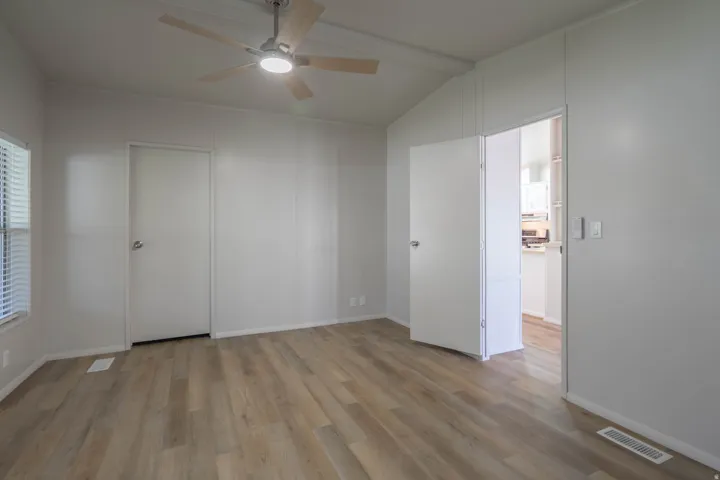 Spacious room featuring wood-finish flooring, light gray walls, an angled ceiling, and a ceiling fan with integrated lighting