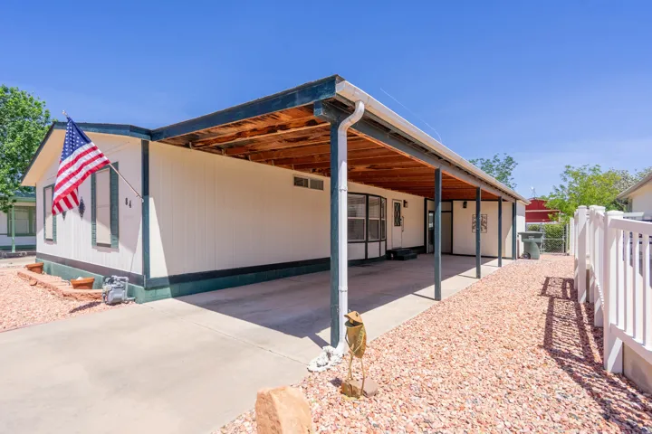 Exterior featuring a covered concrete carport, white siding, dark trim, and a white fence