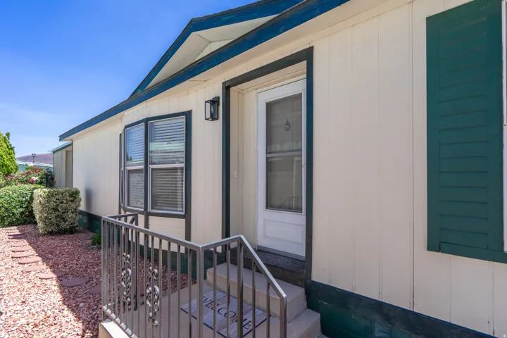 Front exterior featuring white vertical siding with dark green trim, a bay window with blinds, and a white entry door