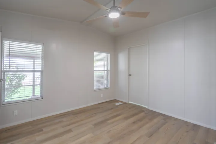 Room featuring light wood-finish flooring, two windows with blinds, a white door, and a ceiling fan with integrated lighting