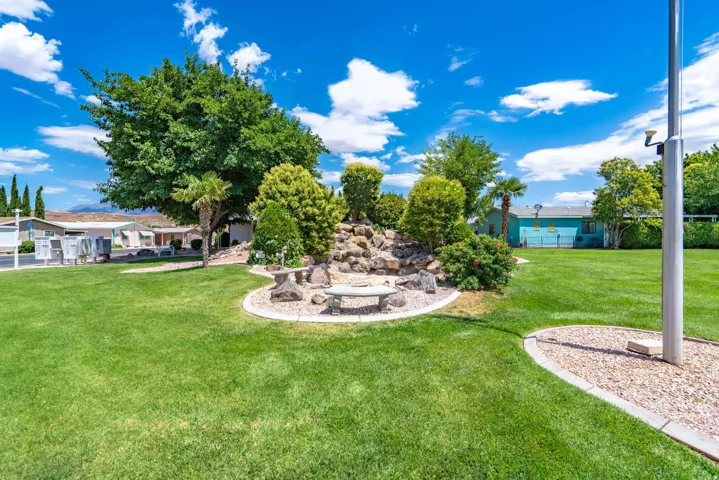 Manicured lawn area featuring a decorative rock garden with mature shrubs and a concrete bench