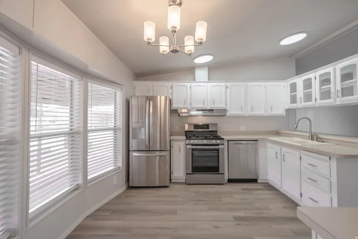 Modern kitchen featuring white cabinetry, stainless steel appliances, wood-finish flooring, and a contemporary chandelier