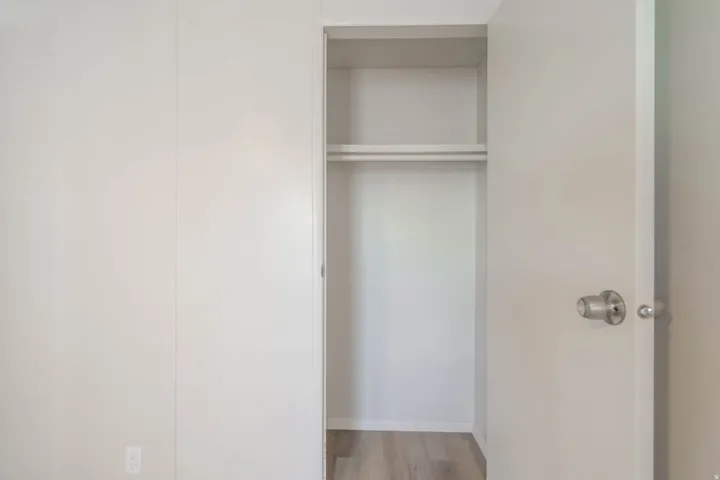 Recessed closet with a single hanging rod and upper shelf, featuring wood-finish flooring