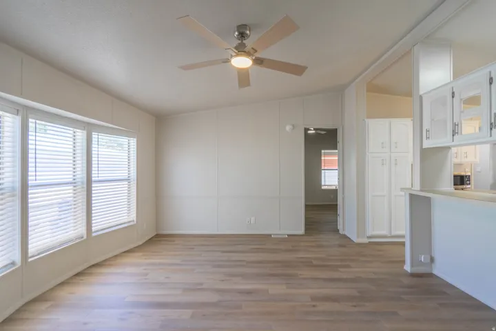 Open concept living area featuring wood-finish flooring, a ceiling fan with integrated lighting, and multiple windows with blinds