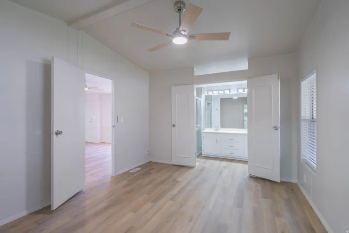 Spacious room featuring light wood-finish flooring, a ceiling fan with integrated lighting, and white paneled walls