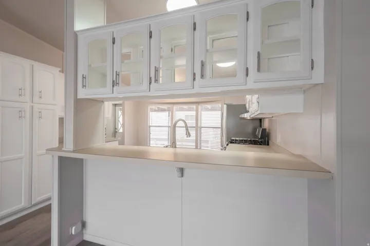 Kitchen pass-through featuring white cabinetry with glass inserts, a single basin sink with a high-arc faucet, integrated cooktop, and a breakfast bar