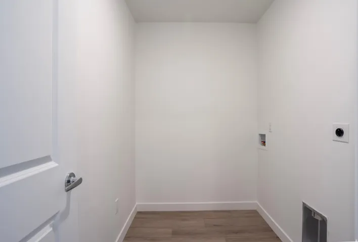 Dedicated laundry area featuring wood-finish flooring, white walls, and essential utility hookups