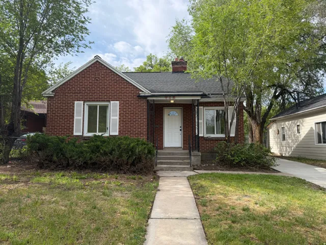 Brick exterior featuring white window shutters, a front porch with black railings, and a concrete pathway