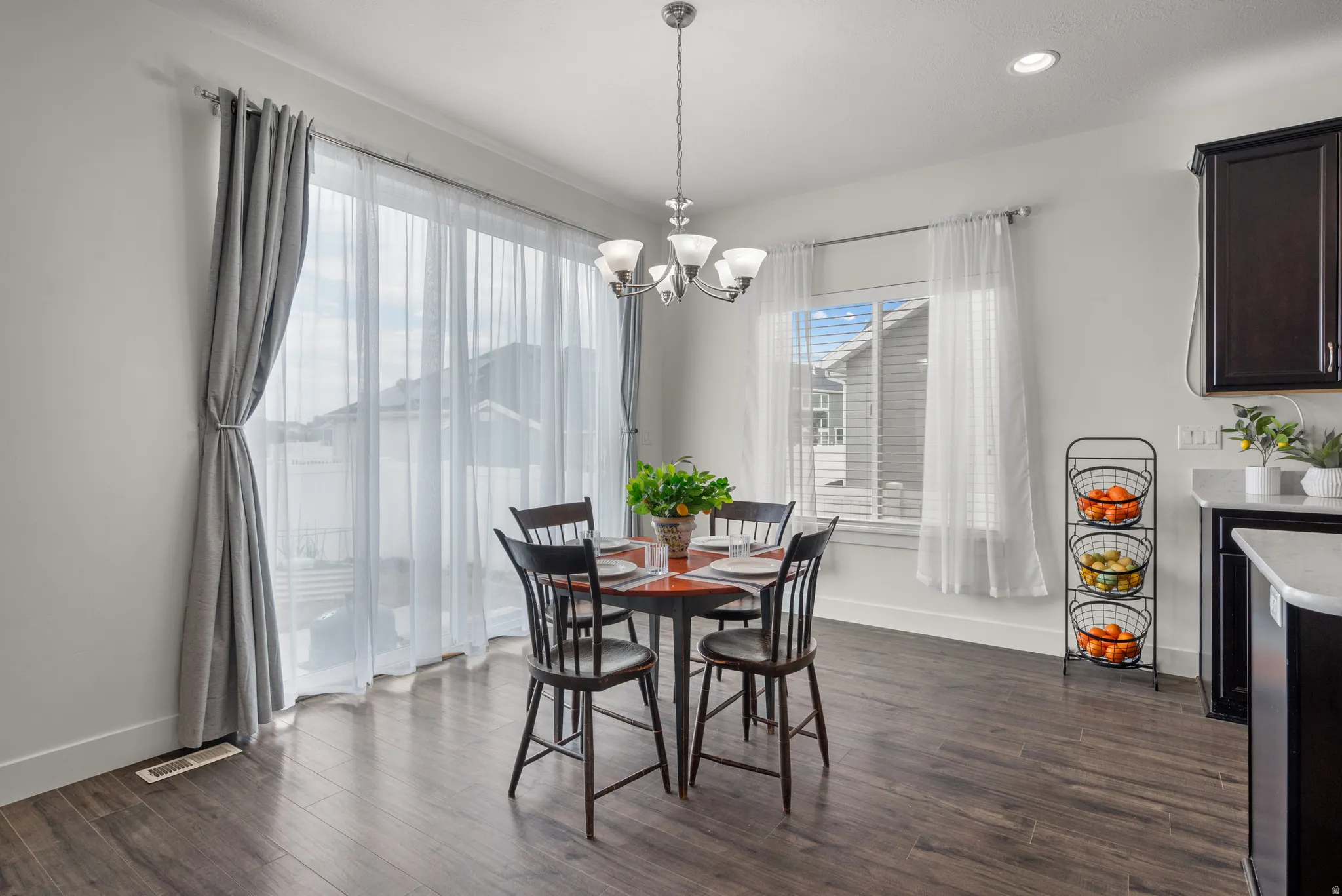 Dining area featuring wood-finish flooring, a contemporary chandelier, and a large window with sheer and blackout curtains