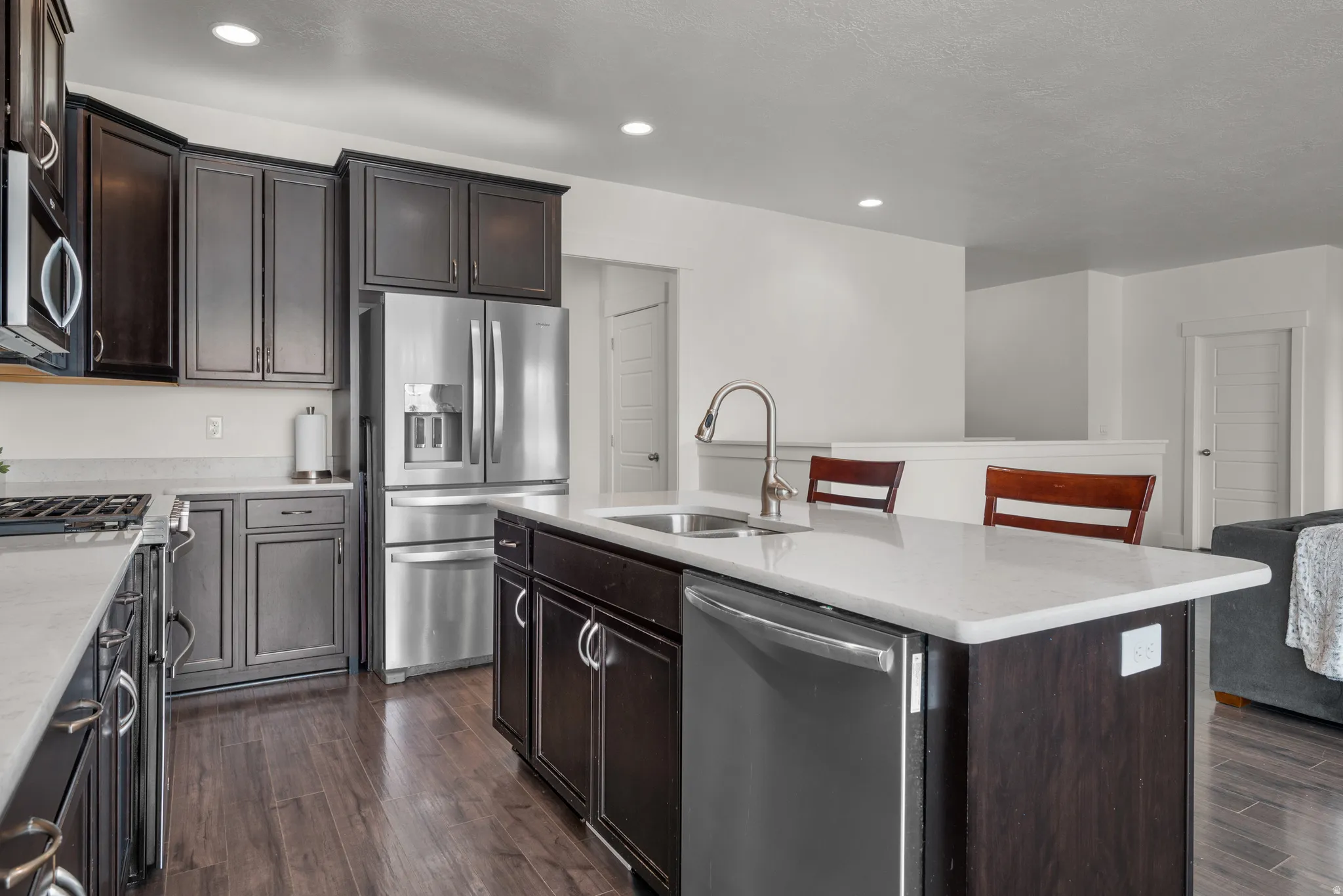 Kitchen featuring upgraded dark wood-finish cabinetry, quartz countertops, stainless steel sink, dishwasher and wood-finish flooring