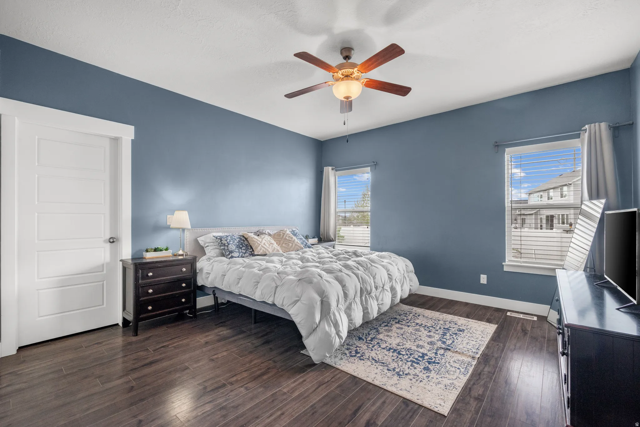 Primary bedroom featuring two windows allowing airy natural light and a ceiling fan with integrated lighting