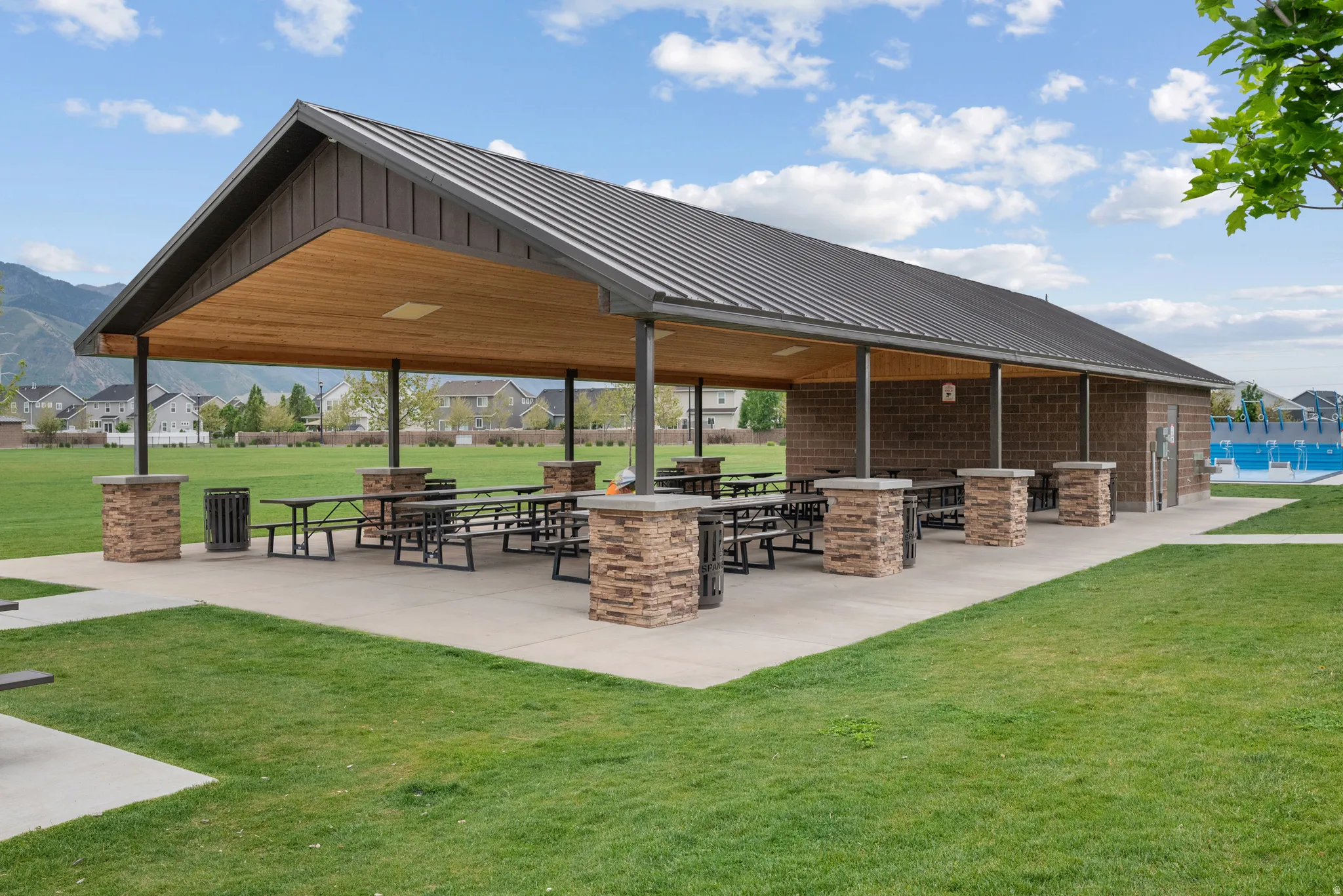 Expansive outdoor pavilion featuring a metal roof and exposed wood-finish ceiling. Fitness equipment on other side and this is adjacent to playground and open area great lawn space.