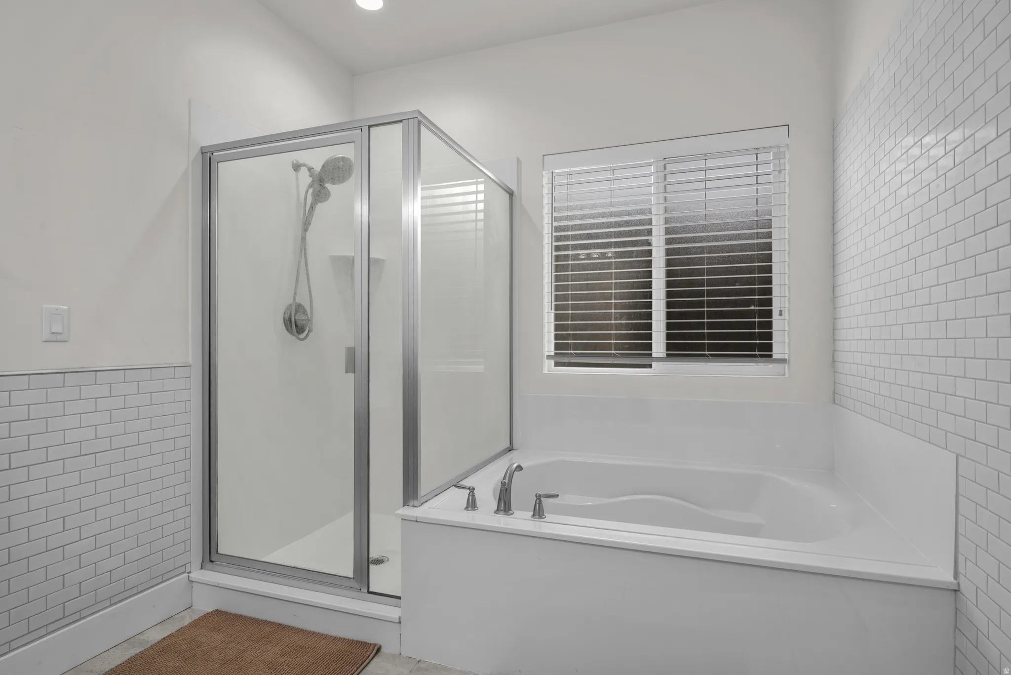 Primary bathroom featuring a luxurius built-in soaking tub with privacy glass window and blinds, a glass-enclosed shower with a handheld shower head, and white subway tile wainscoting