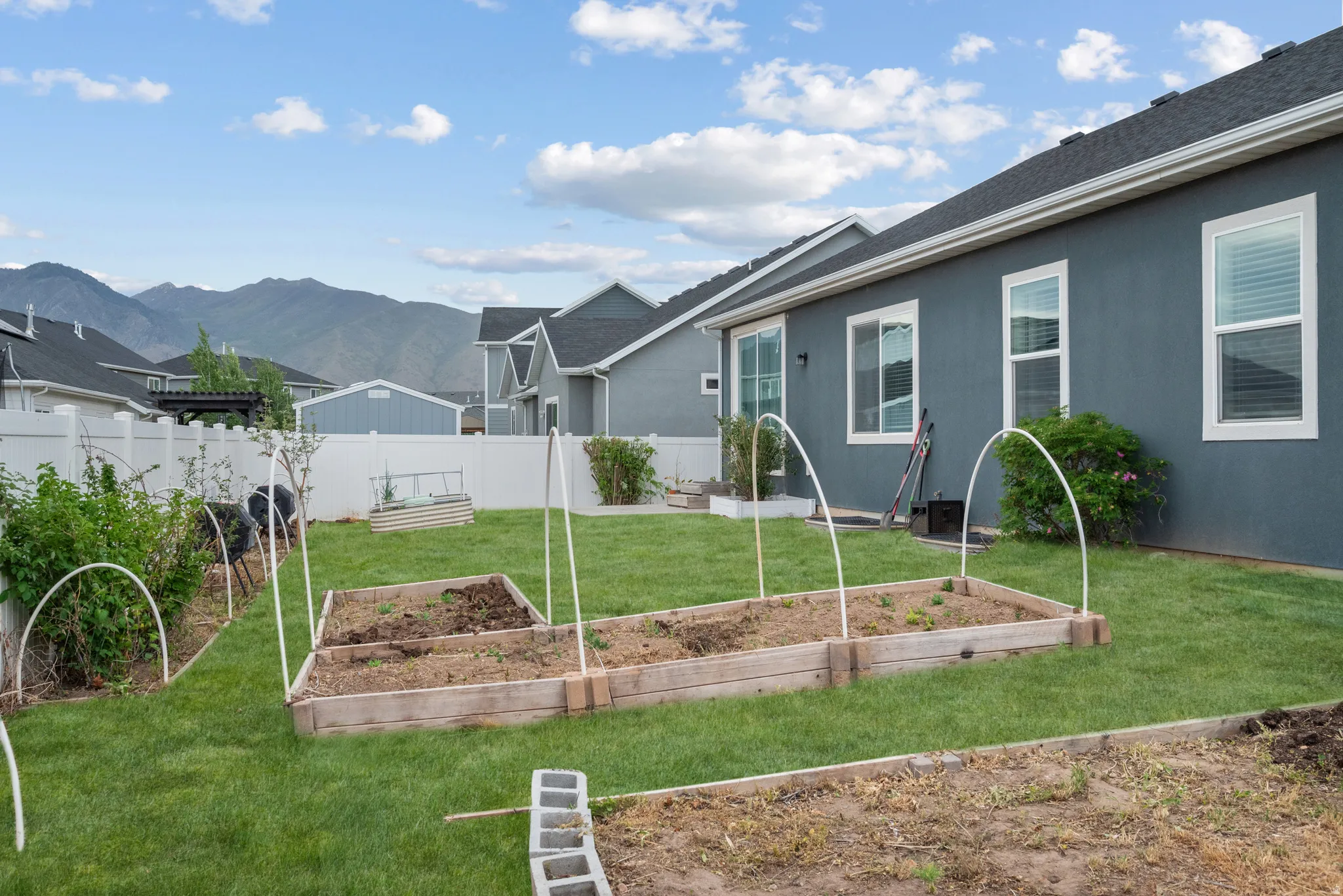 Spacious backyard featuring multiple raised garden beds, and a white vinyl privacy fence and views of Maple Mountain