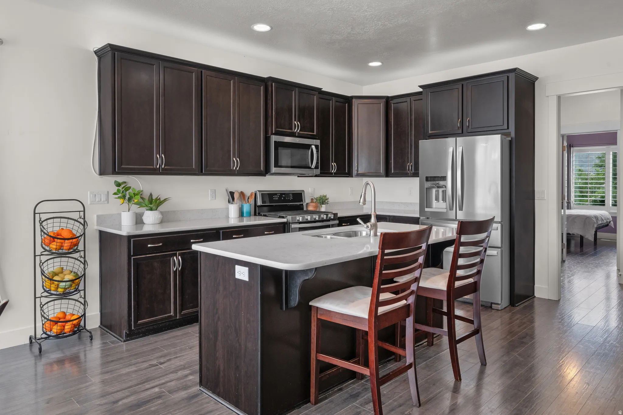 Contemporary kitchen featuring upgraded dark wood cabinetry, above cabinet lighting, light-toned quartz countertops, and stainless steel appliances.