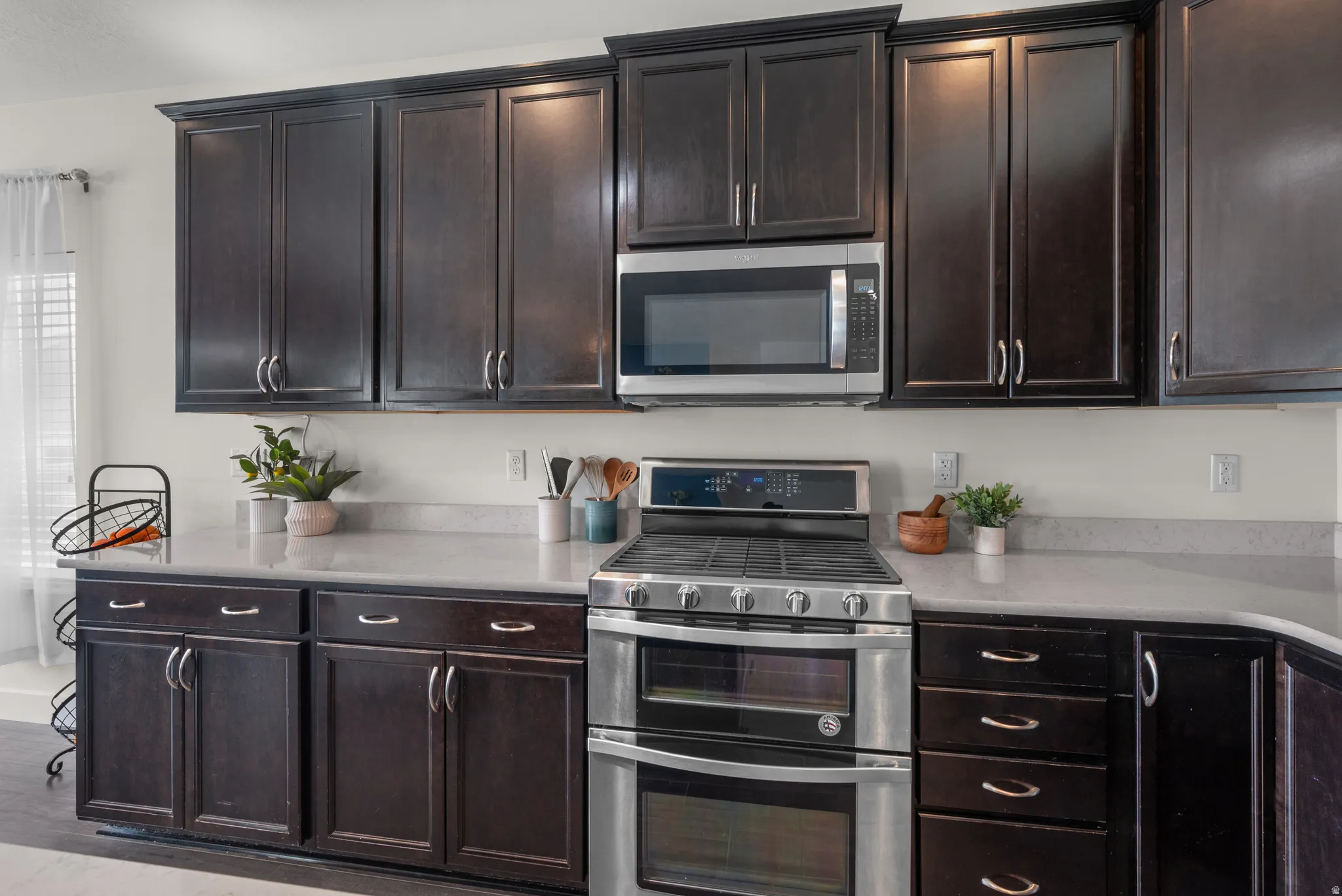 Kitchen featuring dark wood-finish cabinetry, light-toned  quartz countertops, and a stainless steel oven range and gas range with a built-in microwave