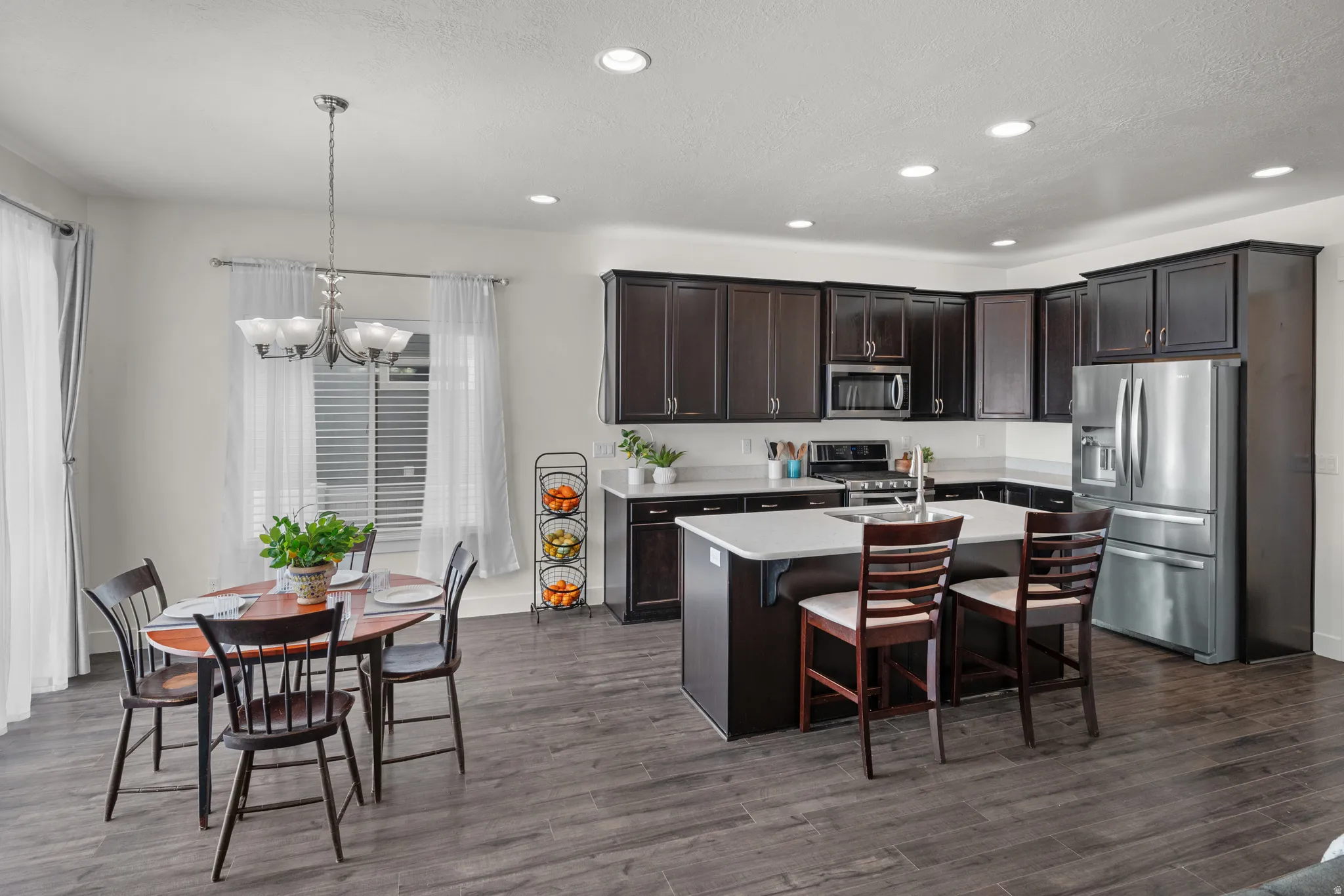 Open-concept kitchen and dining area featuring dark wood-finish cabinetry, with  stainless steel appliances, a center island with seating, recessed lighting, and wood-finish flooring