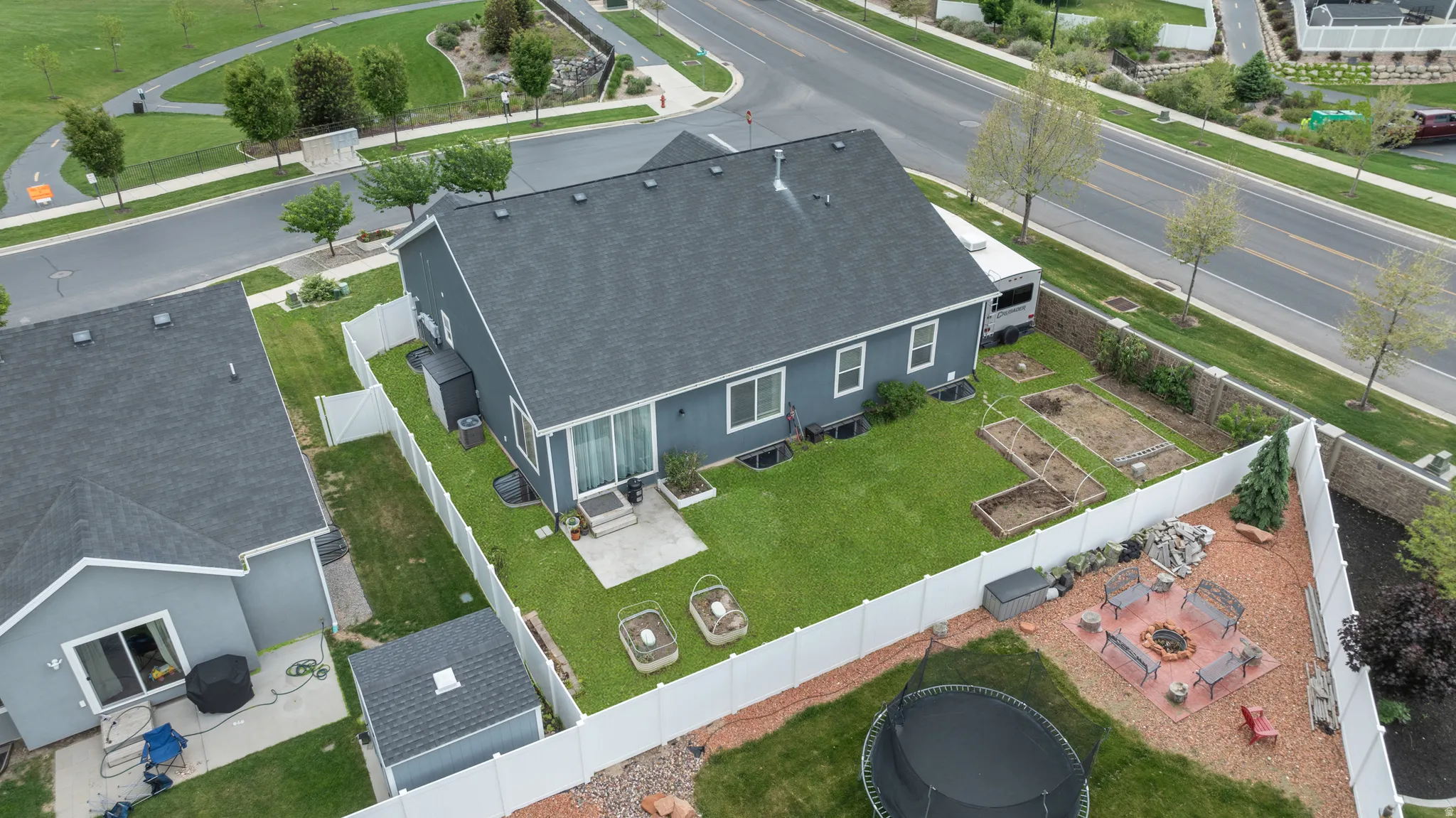 Fenced backyard featuring a concrete patio, expansive yard raised garden beds, and an additional storage shed on the side yard.