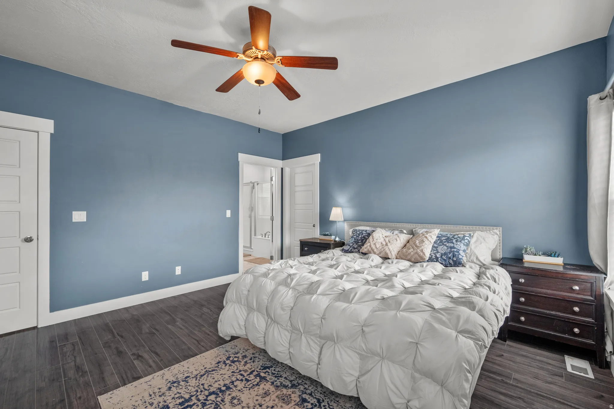 Spacious primary bedroom featuring wood-finish flooring, a ceiling fan with integrated lighting, and a doorway opening to a walk in closet and a primary bath
