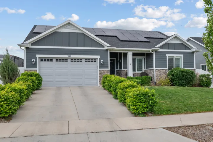 Contemporary ranch-style exterior featuring a dark gray siding, stone veneer accents, an attached two-car garage, and rooftop solar panels. A premium asset,  the fully owned and paid off in full (no lease) solar panels provide 10,000 kilowatts of electric