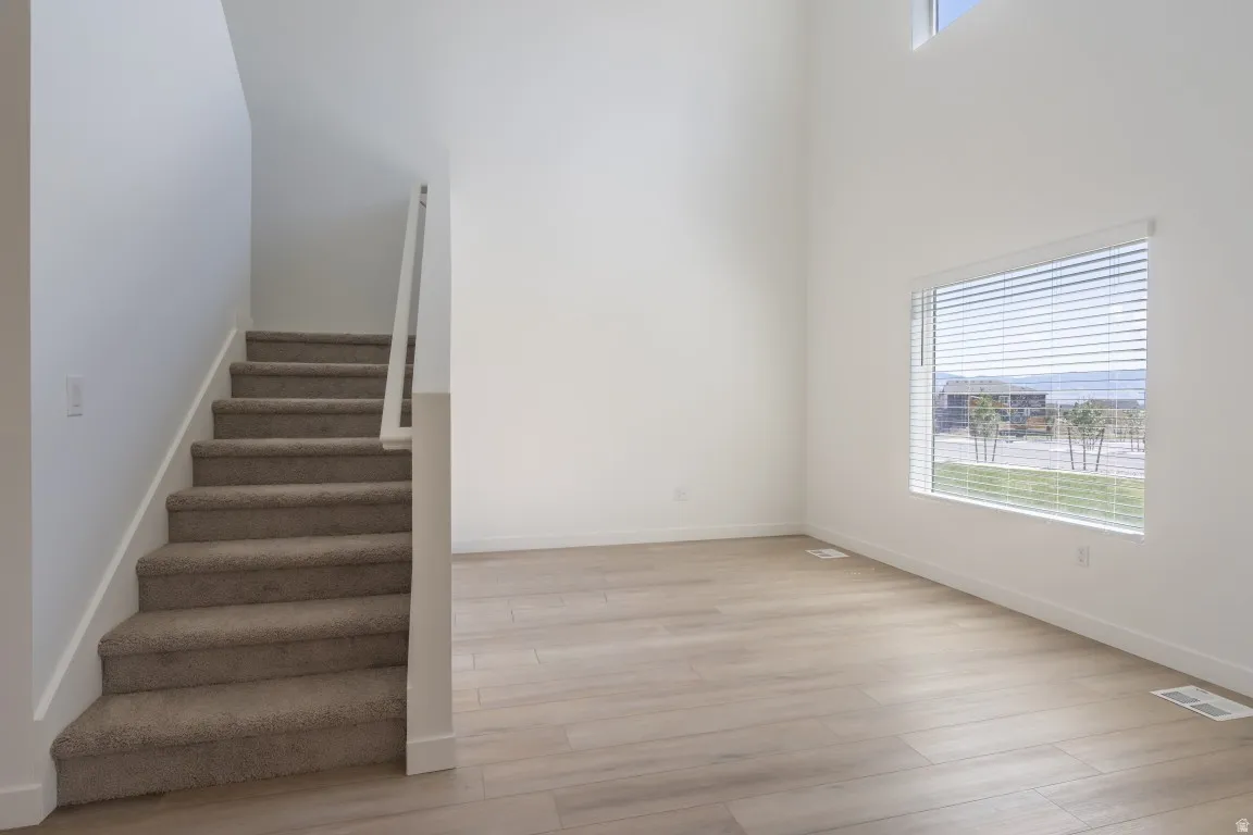 High ceilings with an upper window, wood-finish flooring, and a large window with horizontal blinds