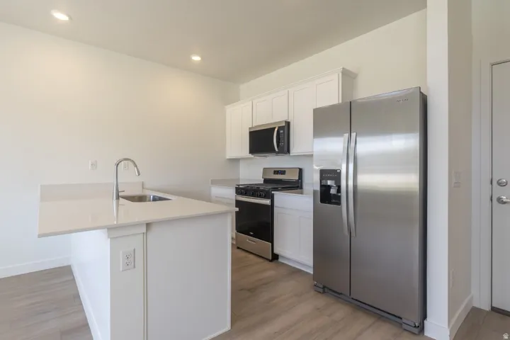 Kitchen featuring an island with a stainless steel sink and gooseneck faucet, light-toned countertops, white cabinetry, and stainless steel appliances