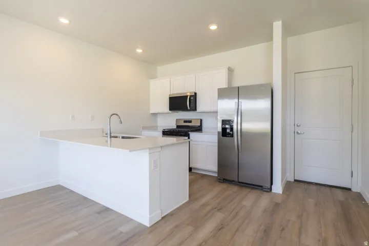 White cabinetry, stainless steel appliances, recessed lighting, wood-finish flooring, and a kitchen island with sink and integrated breakfast bar