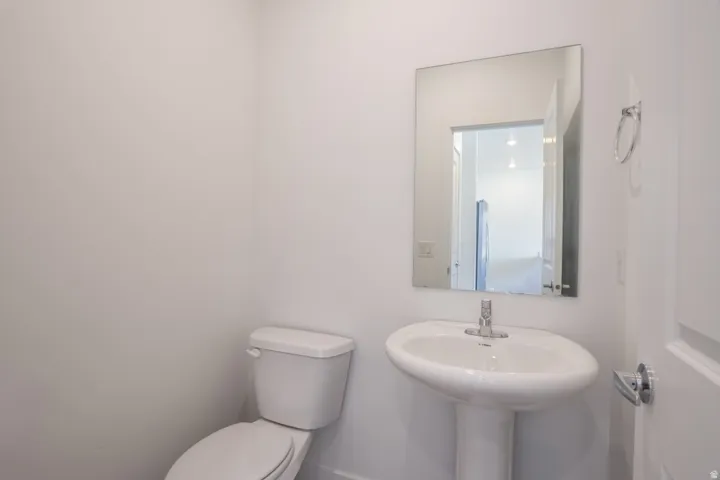Pedestal sink with chrome faucet, wall-mounted mirror, and white toilet