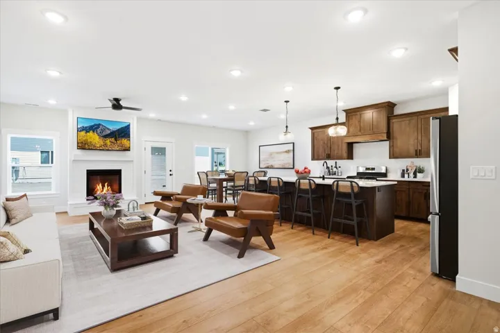 Spacious open-concept living area featuring wood-finish flooring, a white brick fireplace with a mantel, and recessed lighting