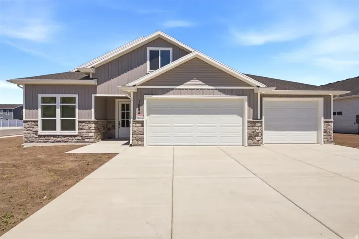 Modern exterior featuring gray vertical and horizontal siding, stone veneer accents, an attached three-car garage, white frame windows, and a concrete driveway