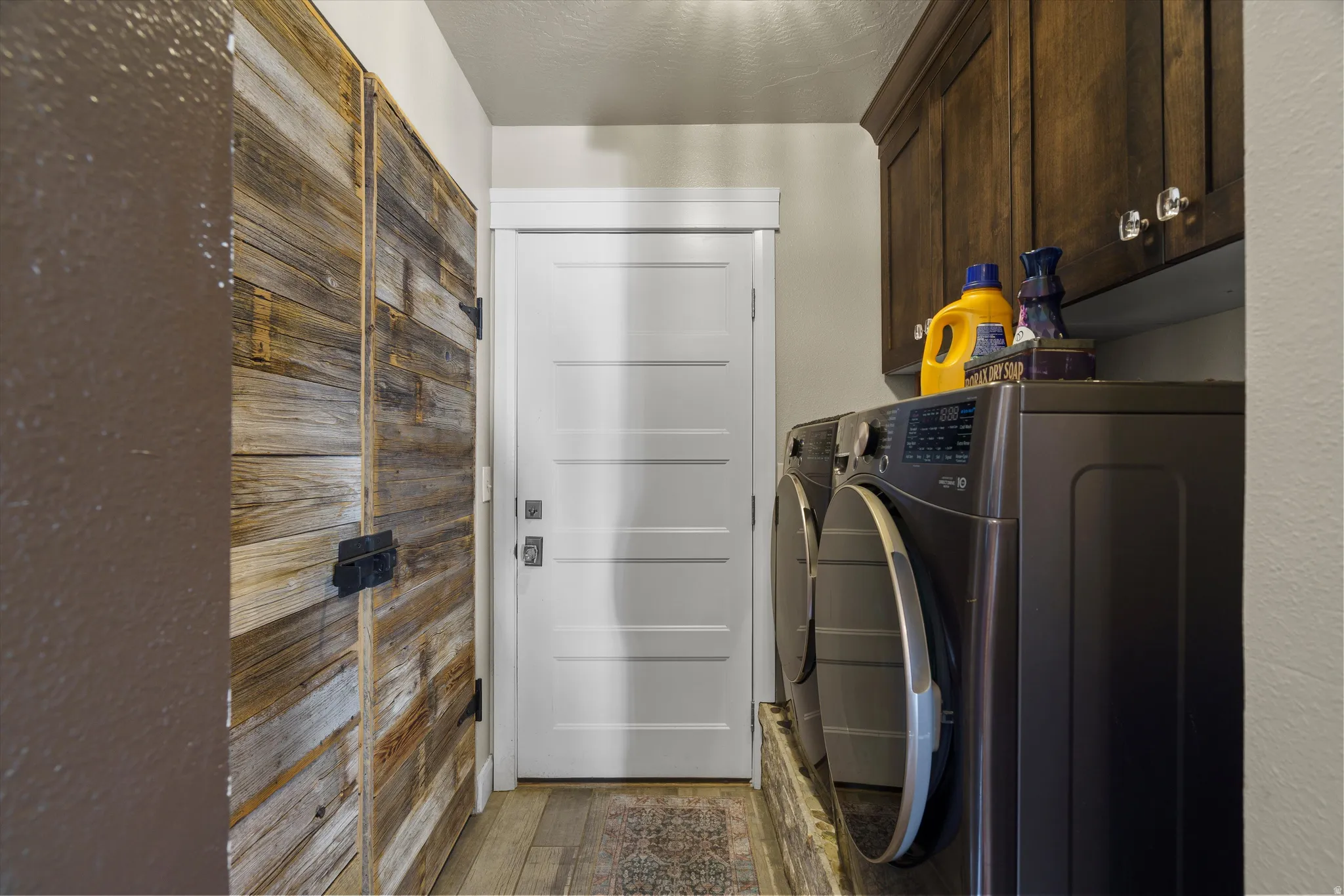 Dedicated laundry area featuring dark wood-finish cabinetry, modern front-load appliances, a white paneled door, and wood-finish flooring