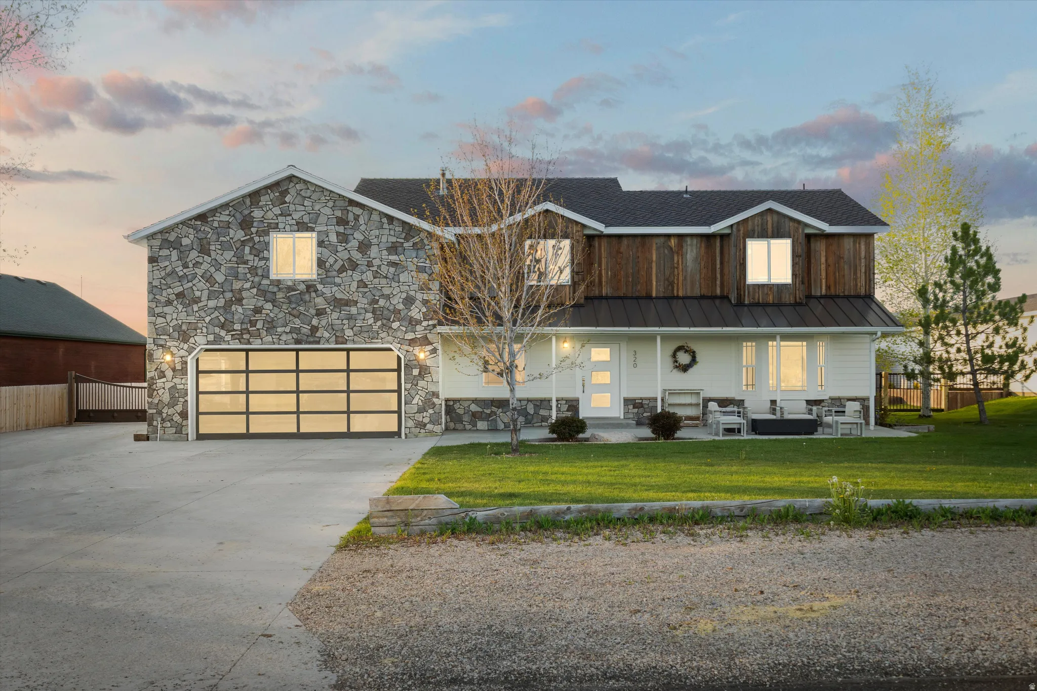 Stone and wood-sided exterior featuring a modern glass panel garage door, covered front porch, white door with vertical glass inserts, and a manicured lawn