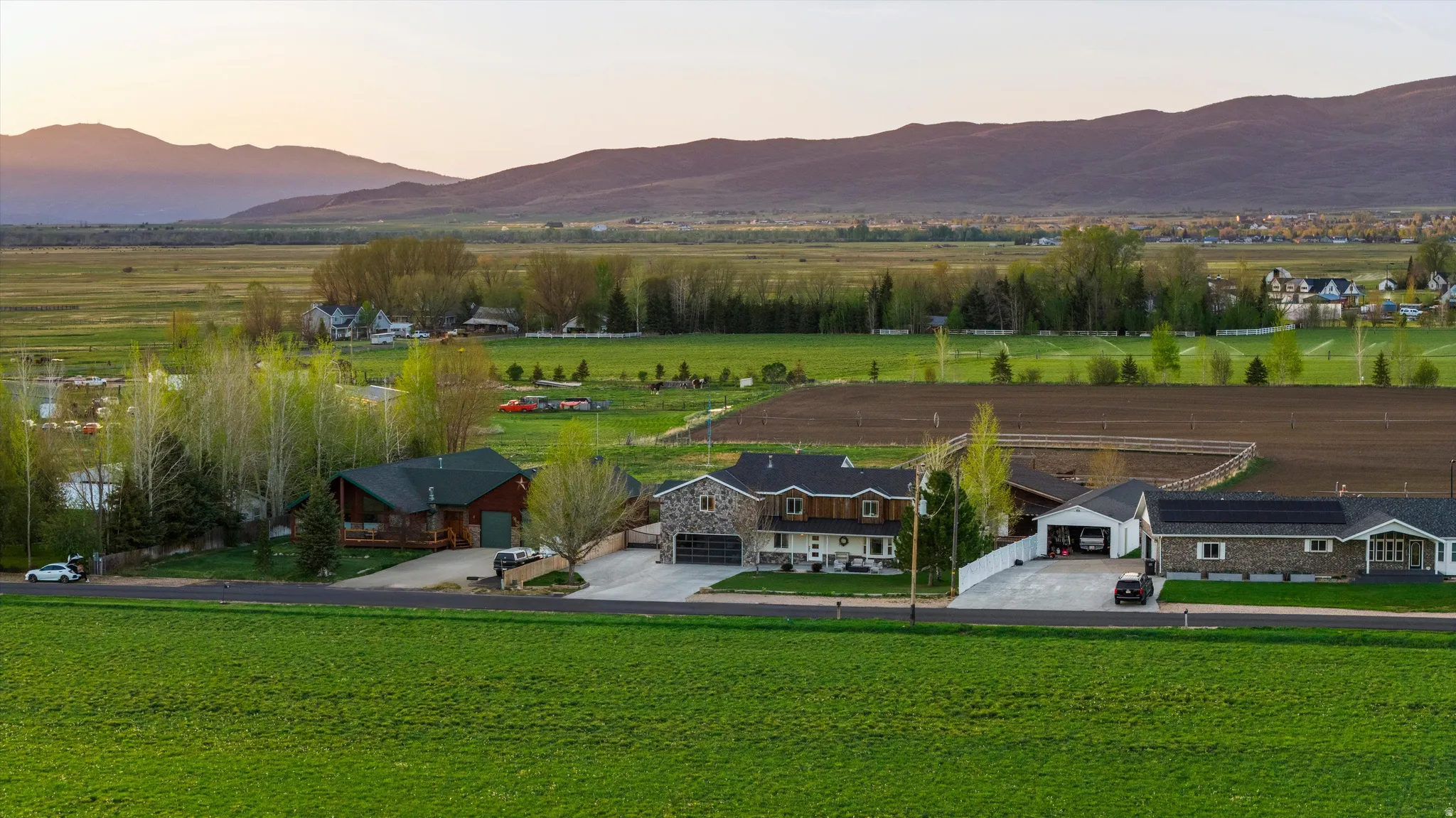 Expansive green fields surrounding multiple properties with mountain range backdrop