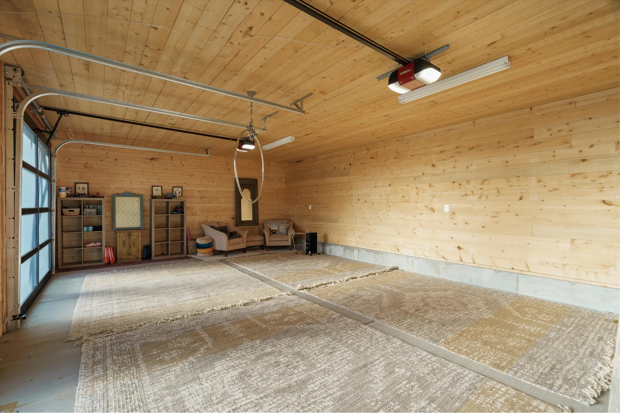Spacious interior featuring natural wood plank walls and ceiling, a full-panel glass garage door, and durable concrete flooring with distinct sections