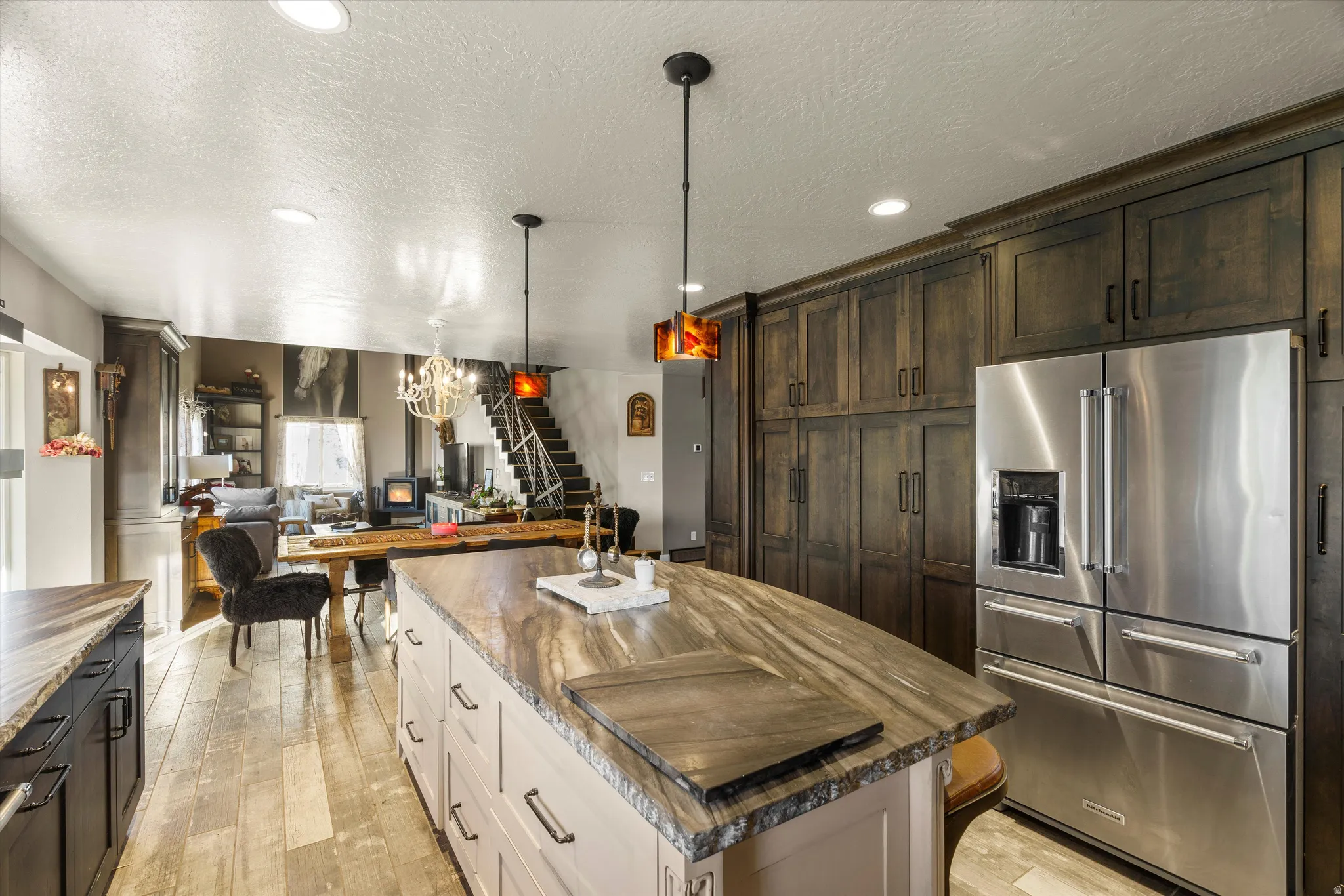 Kitchen featuring an expansive island with a light-toned base and a dark-toned stone countertop, wood-finish flooring, recessed ceiling lighting, and pendant lighting