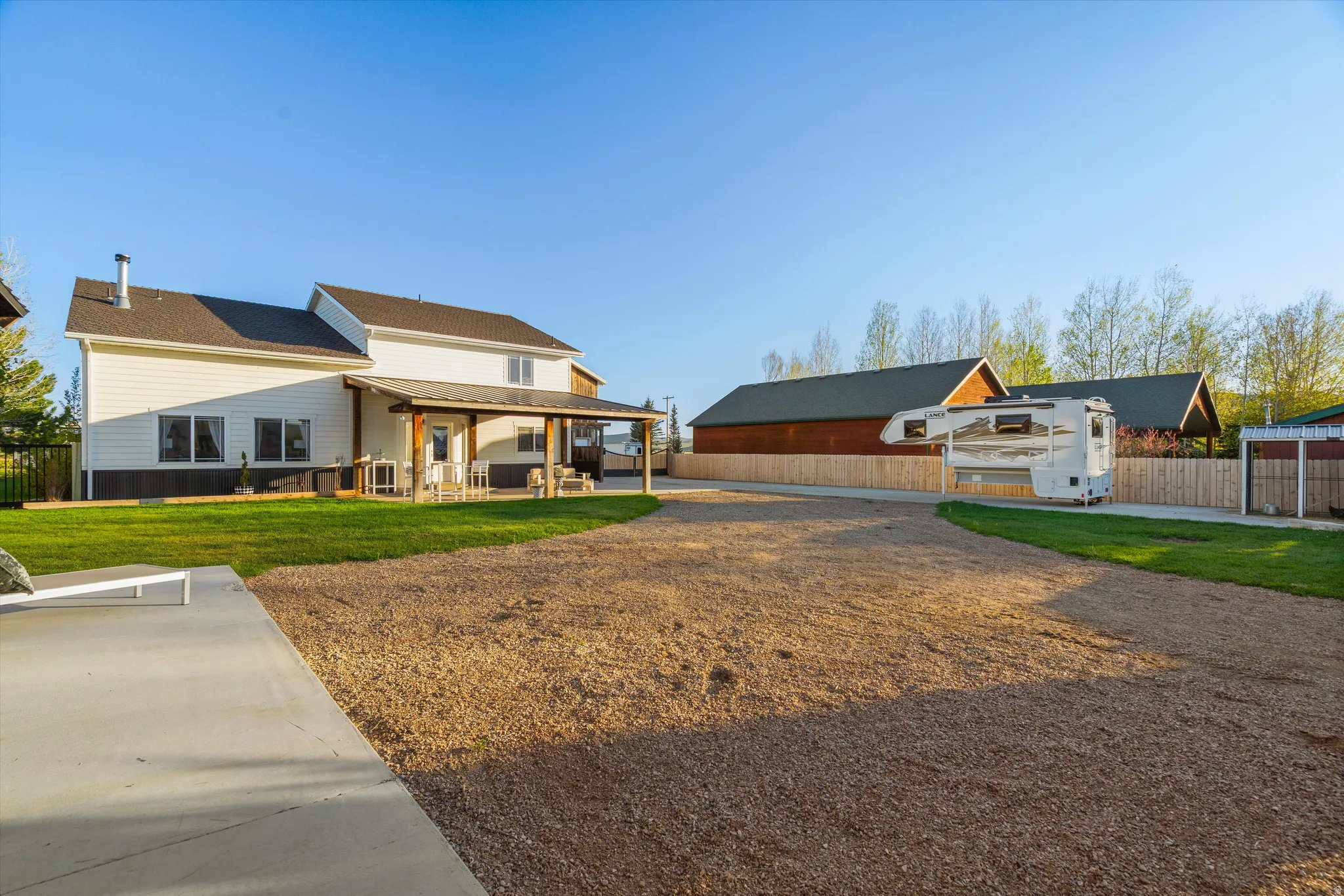 Spacious gravel driveway with an expansive rear patio, featuring a covered porch with wooden beams
