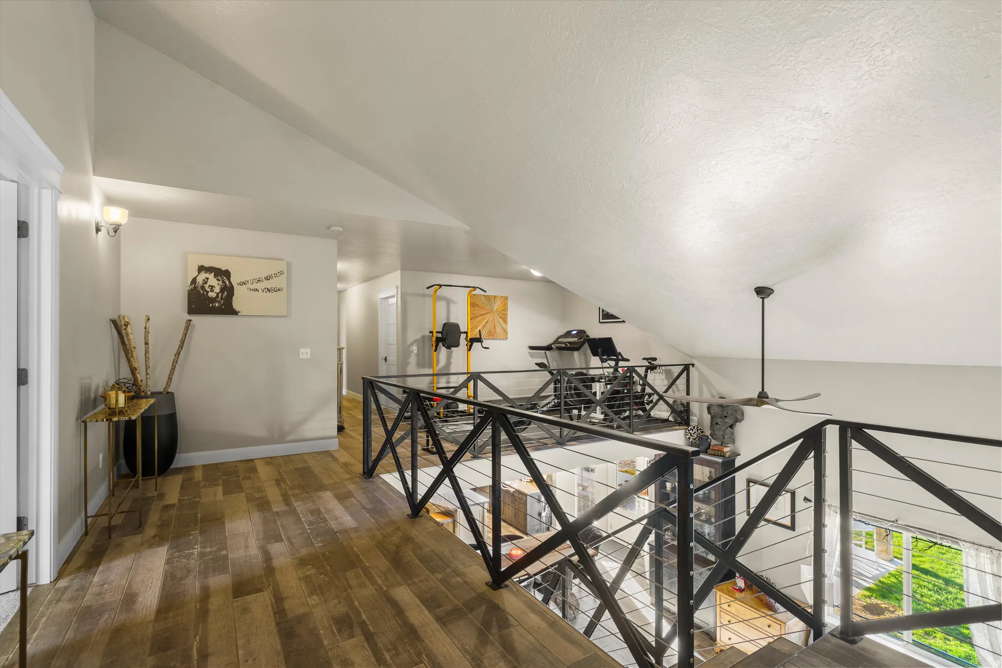 Open loft area with wood-finish flooring, vaulted ceilings, and a contemporary black metal railing with cable infill
