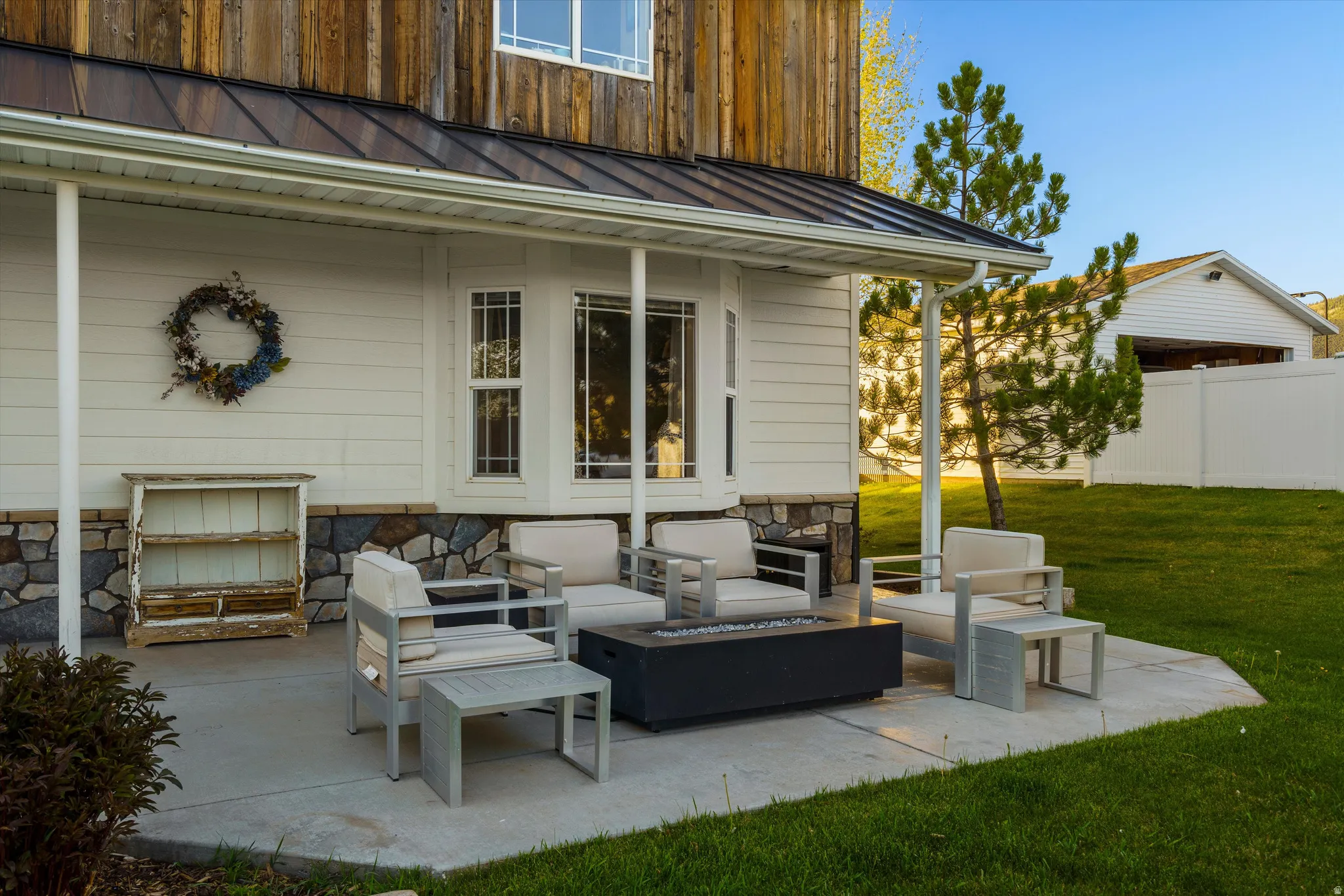 Covered patio with a concrete slab, white siding, stone foundation accents, and a metal roof