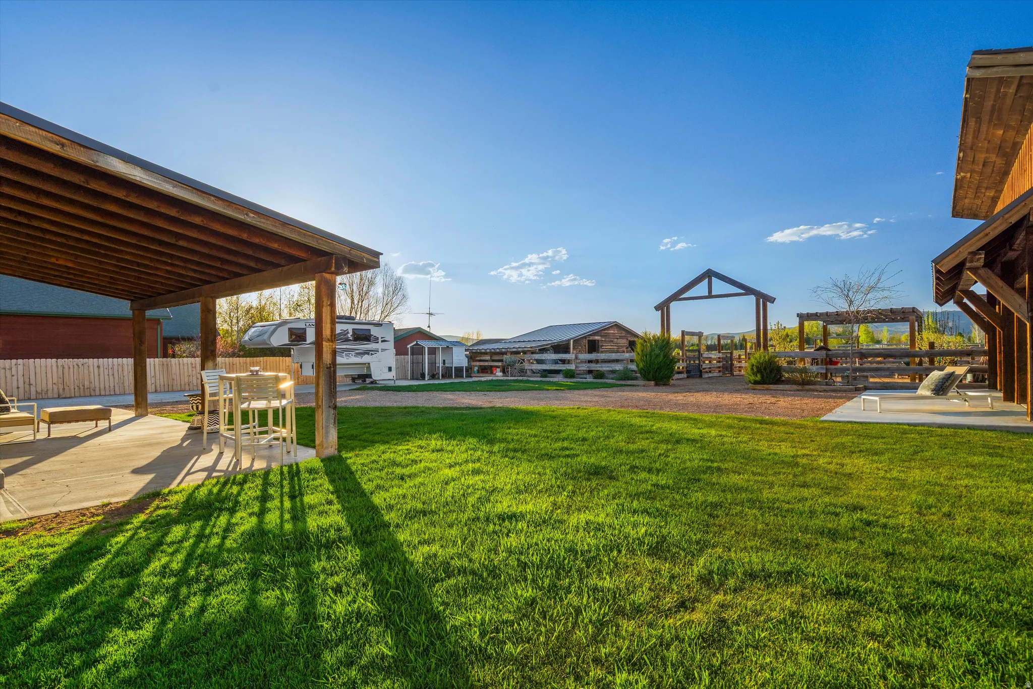 Expansive outdoor space featuring a covered patio, a large grassy area, a gravel pathway, a wooden pergola, and a visible barn structure