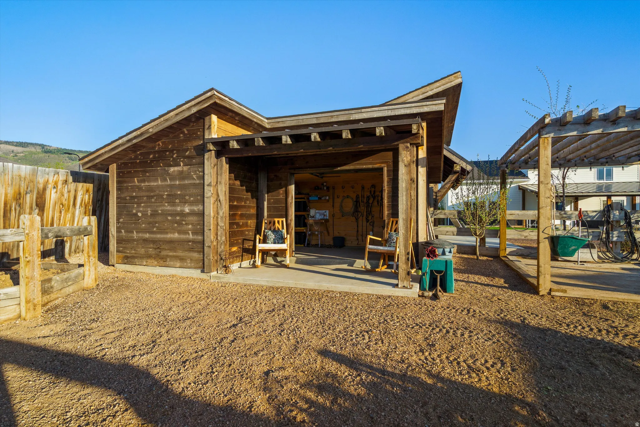 Wood-sided outbuilding with an open-air covered patio area, featuring a sloped roofline and a wooden pergola structure