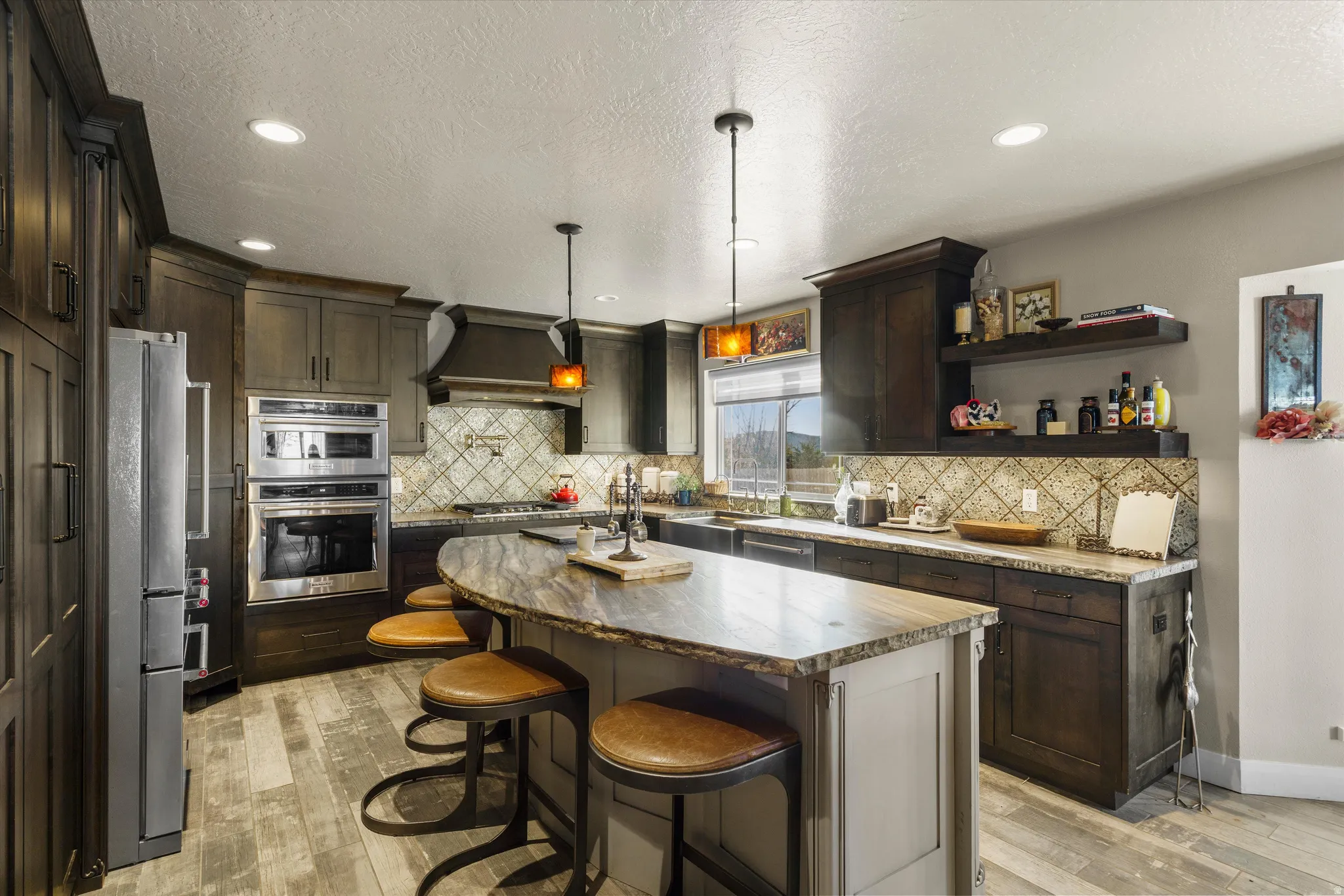 Gourmet kitchen featuring a curved island with seating, stainless steel double ovens, wood-finish flooring, recessed lighting, and ample cabinetry
