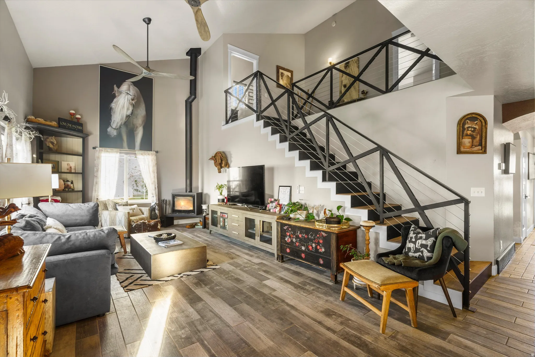 Vaulted living space featuring wood-finish flooring, a contemporary metal staircase with cable railing, and an exposed pipe stove