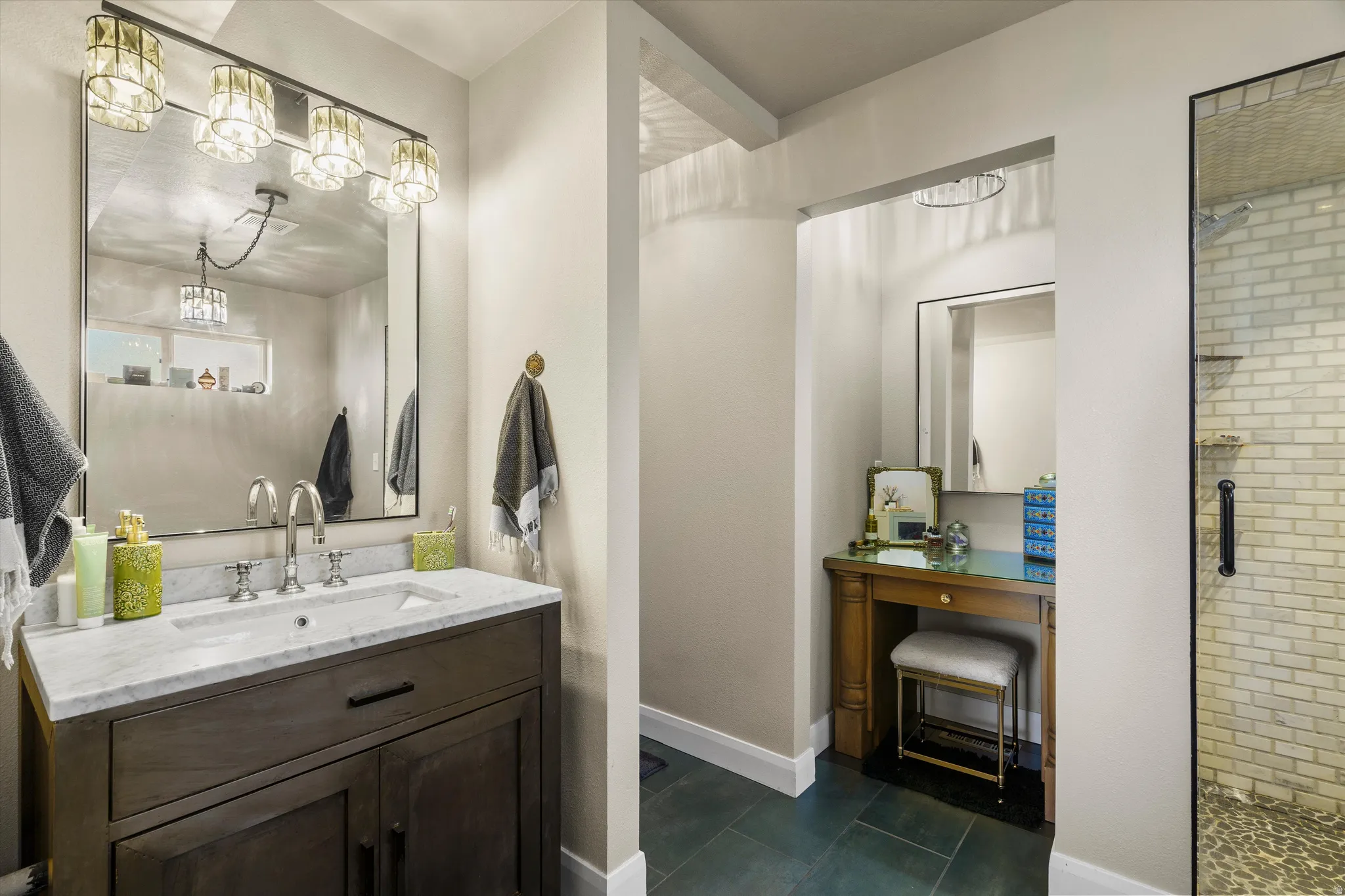 Bathroom featuring a dark wood vanity with a white countertop and a rectangular undermount sink, a large mirror with integrated lighting, and a glass-enclosed shower with subway tile walls