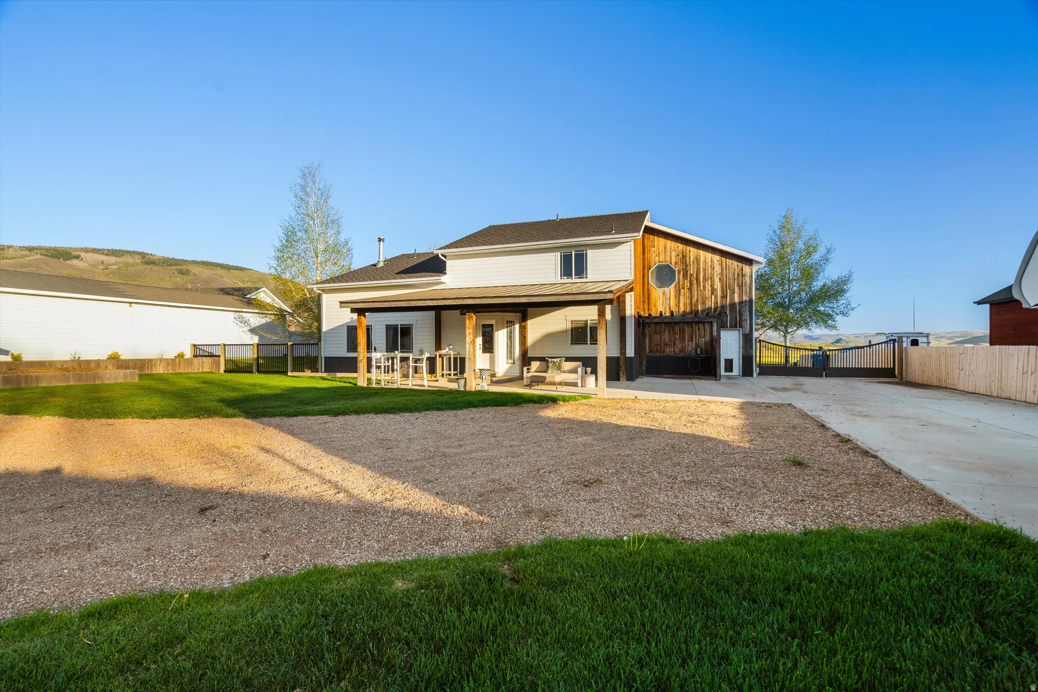 Rear exterior featuring a covered patio with wood columns, a gravel parking area, and a large grassy yard